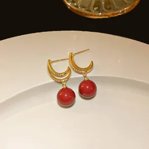Close-up of gold-plated crescent earrings with vibrant red spherical beads and crystal accents.