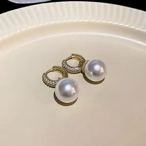 Close-up of elegant gold-plated earrings featuring cubic zirconia and large pearls.