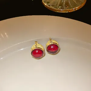 Close-up of elegant red stone gold-plated stud earrings resting on a white ceramic plate.