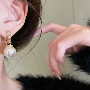 Close-up view of elegant gold plated zircon and white pearl hoop earring worn on ear