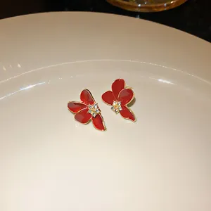 Detail shot of red enamel flower stud earrings with a sparkling rhinestone center.