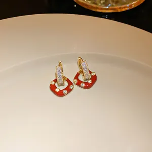Detailed view of red enamel heart earrings with crystal accents on a beige plate