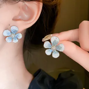 Detailed close-up of light blue flower stud earrings with sparkling crystal centers on ear