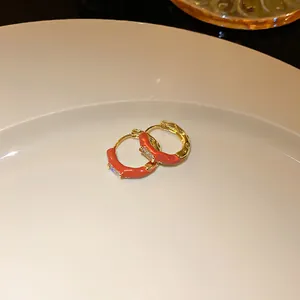 Detail view of gold-plated hoop earrings with orange enamel and clear stones on a white plate.