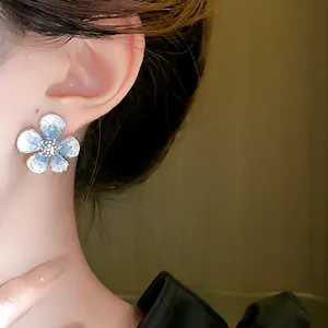 Detailed close-up showing elegant blue flower stud earring with crystal center on model