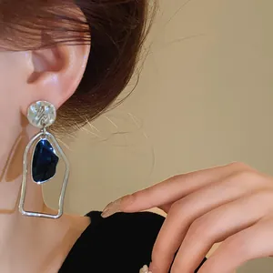 Dettaglio ravvicinato di orecchini geometrici in argento con goccia di resina blu scuro