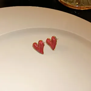 Macro view of elegant red heart-shaped stud earrings on a minimalist white ceramic plate