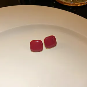 Close-up of elegant square burgundy red stud earrings with gold trim on a white plate