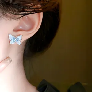 Detailed view of an elegant blue and white butterfly stud earring worn on model's ear
