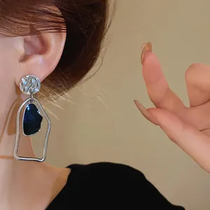 Primo piano di orecchini geometrici in argento e nero indossati da una modella.
