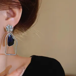 Dettaglio di orecchini argentati irregolari con smalto blu indossati da modella.