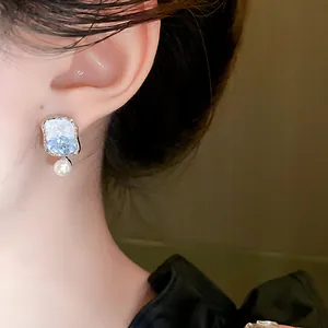 Detailed view of elegant square blue crystal and pearl drop earrings on a model's ear