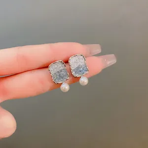 Close-up of elegant square crystal stud earrings with pearl drop on silver needle.