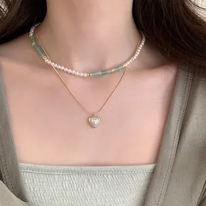 Close-up of a double-layered baroque pearl necklace with a gold heart pendant on a model.