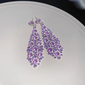 Primo piano di orecchini pendenti in zircone viola con forma a rombo irregolare.
