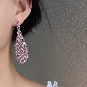 Primo piano di orecchini pendenti a rombo irregolare con zirconi rosa indossati.