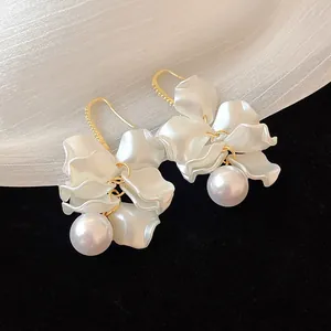 Close-up of elegant flower petal earrings with large white pearls and gold hooks.