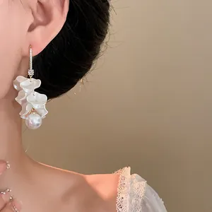 Close-up detail of elegant white petal tassel earrings with a pearl worn on a model's ear