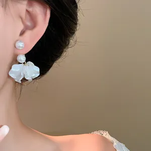 Detailed view of elegant pearl and white flower petal drop earrings worn on a model ear