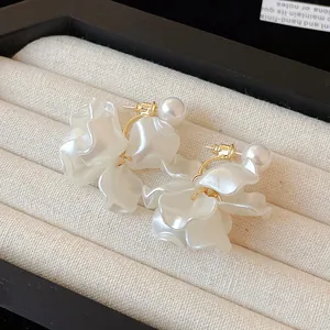 Detail of elegant 18K gold plated earrings with pearls and white flower petals.