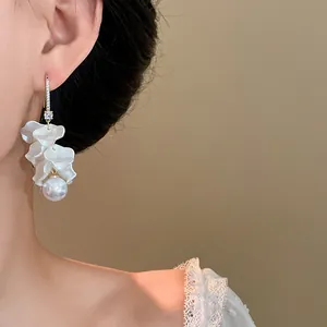 Close-up of elegant white flower petal tassel earrings with a dangling pearl on a model.