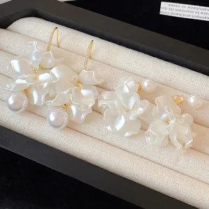 Detail of 18K gold plated pearl flower earrings on a beige velvet display tray.
