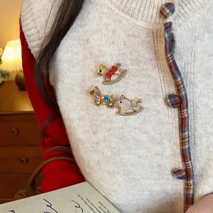 Detailed macro shot of three rhinestone enamel rocking horse brooches pinned on a white knit vest.
