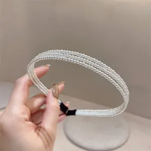 Detailansicht des eleganten, dreilagigen weißen Perlenhaarbands, in der Hand gehalten.
