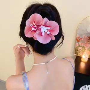 Detail view of an elegant pink fabric orchid hair clip with pearl worn on dark hair