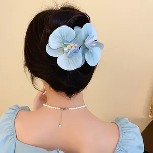 Detailed view of blue fabric orchid hair clip with central pearl on model's hair