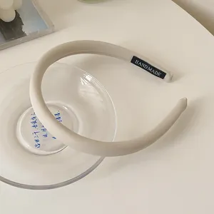 Nahaufnahme eines beigen gepolsterten Schwamm-Stirnbands mit schwarzem 'HANDMADE' Webetikett