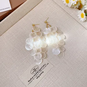 Detailed macro view of white shell disc cluster tassel earrings with golden studs