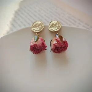 Exquisite close-up of romantic dried pink rose bud drop earrings with gold textured studs.
