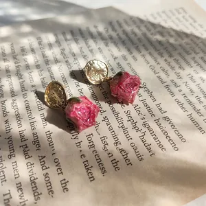 Detail view of preserved rose earrings on a book with soft sunlight shadows.