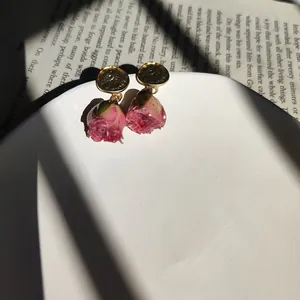 Detailed macro view of handmade preserved rose earrings with gold hammered discs.