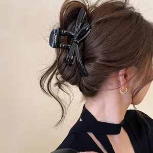 Close-up detail of a large glossy black bow-knot hair claw clip styled in an elegant bun
