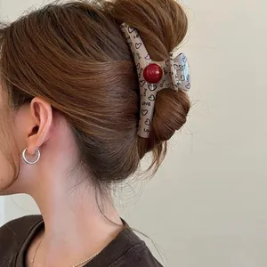Close-up of a vintage coffee hair claw clip with heart prints and red bead on a bun