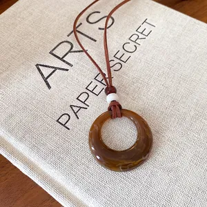 Close-up of retro brown acrylic hollow ring pendant necklace on white linen background