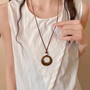 Close-up of a retro amber acrylic circular pendant necklace worn over a white top.