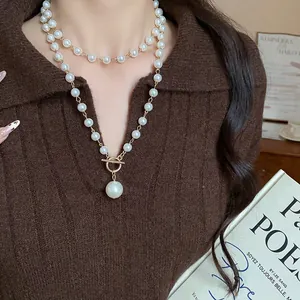 Collana di perle vintage a strati con chiusura OT e pendente su maglione marrone