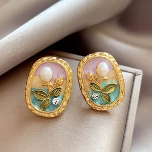 Detailed close-up of elegant gold oval earrings featuring enamel flower, pearl and rhinestone
