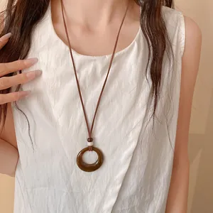 Close-up of retro brown acrylic circular hollow pendant necklace worn on white top