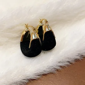 Primo piano di eleganti orecchini a cerchio a forma di U floccati oro e neri da donna.