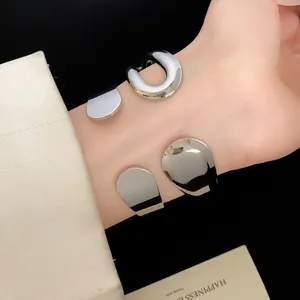 Close-up detail of a minimalist metal teardrop open cuff bracelet worn on a wrist.