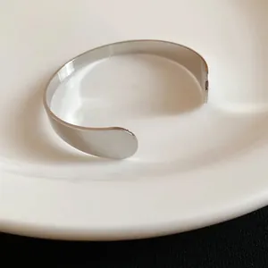 Macro view of a polished silver teardrop open cuff bracelet on a white porcelain plate
