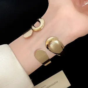 Close-up of vintage minimalist gold metal teardrop and U-shape open cuff bracelets on wrist