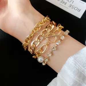 Close-up of layered gold-tone bracelets with pearl and rhinestone details on a wrist.