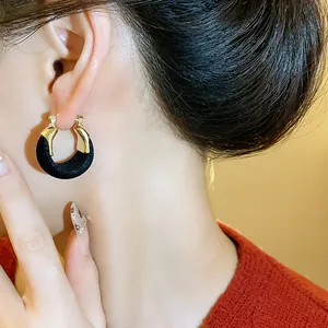 Dettaglio di un orecchino a U dorato con texture floccata nera indossato da una modella