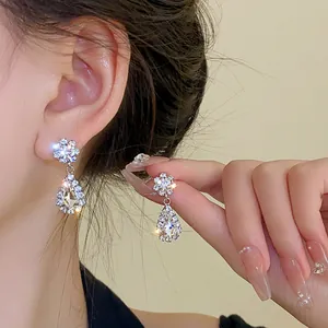 Detailed view of silver-tone flower and pear-shaped rhinestone drop earrings on model