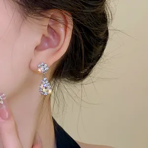 Close-up view of an elegant sparkling floral stud with a teardrop dangle earring on ear